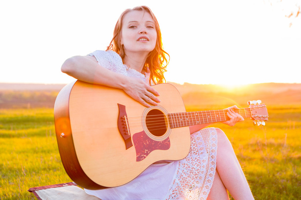 Beautiful young girl playing guitar in the field.  - Photo, image