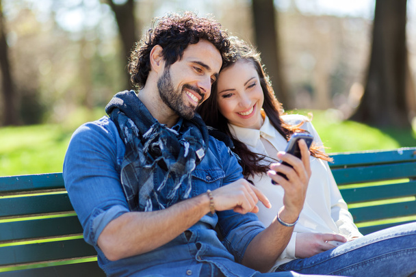 couple using smartphone while sitting on bench - Foto, imagen