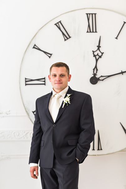 Mann im schwarzen Anzug mit großer Uhr im Hintergrund, Zeitkonzept - Foto, Bild