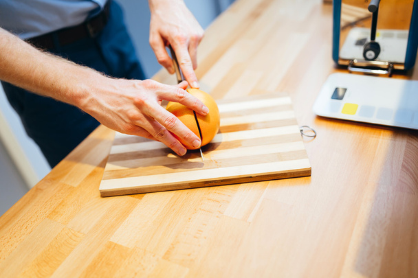 Man slicing orange in kitchen - Zdjęcie, obraz