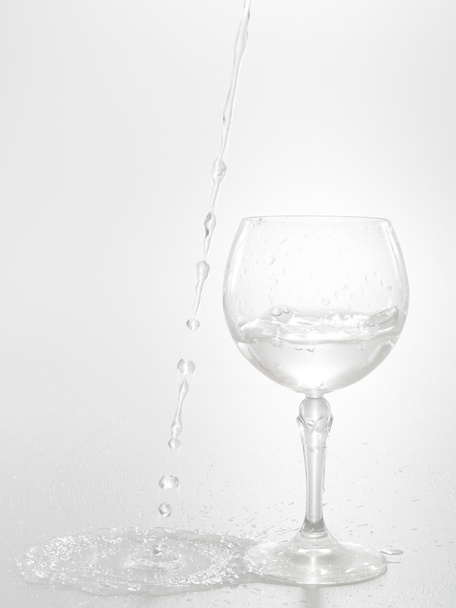 Ροή του νερού έξω από το ποτήρι κρασί που απομονώνονται σε λευκό - Φωτογραφία, εικόνα