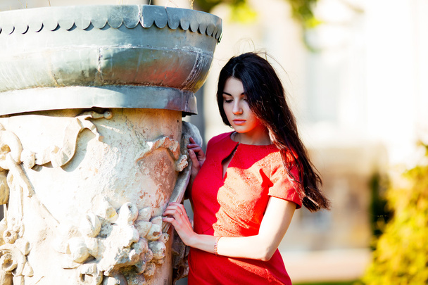 Young pretty beautiful woman walking in the old town and looking to the side. Stylish girl in a red blouse poses outdoors - Foto, Imagen