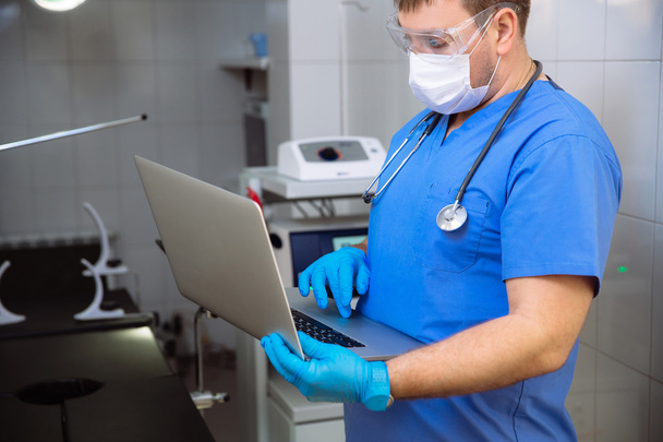 adult doctor in mask with laptop and medical tools in operating room at the hospital - Foto, immagini