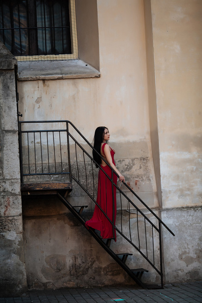 Young beautiful and very elegant woman in a long black evening dress posing on the stairs, photo from the back - Fotó, kép