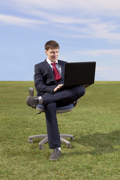 Businessman sitting on chair with a laptop on green meadow - Fotoğraf, Görsel