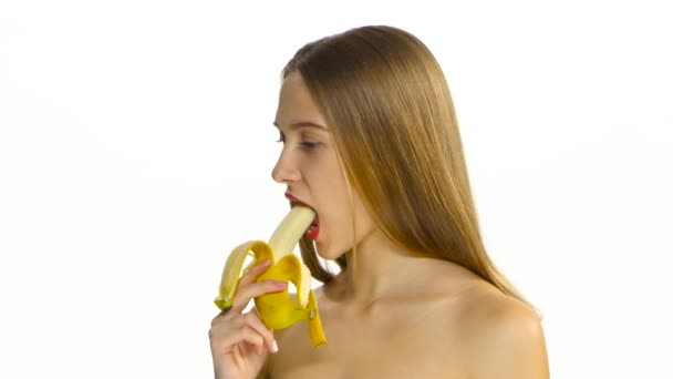 Το κορίτσι με τα σιδεράκια τρώει μια μεγάλη μπανάνα. Λευκό. Closeup - Πλάνα, βίντεο
