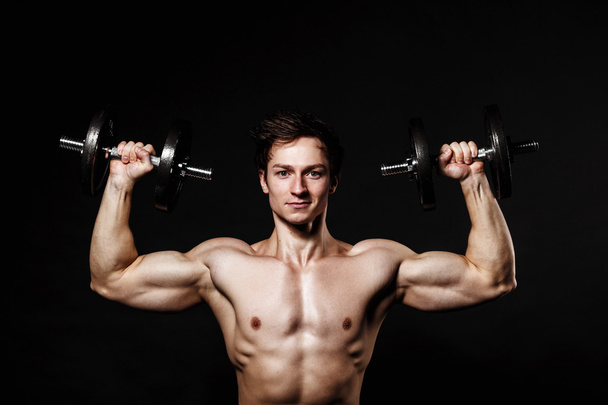 Handsome athletic man with dumbbells confidently looking forward - Foto, imagen