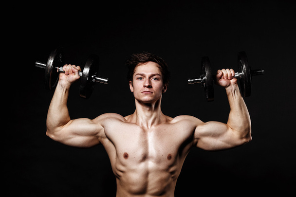 Handsome athletic man with dumbbells confidently looking forward - Fotó, kép