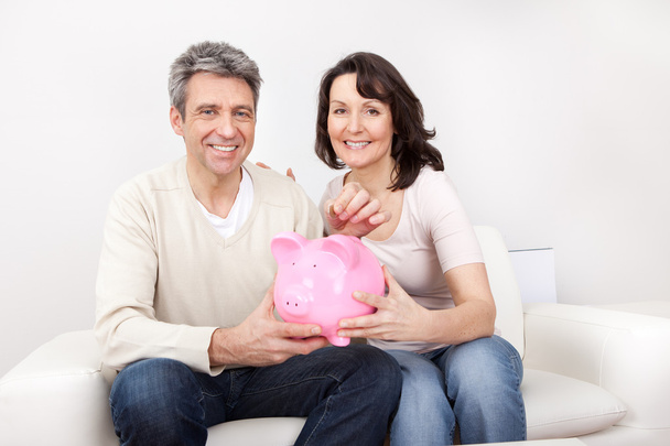 Mature couple saving money in piggybank - Foto, afbeelding