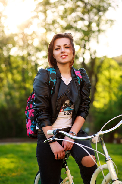 夕日に緑豊かな公園で自転車に乗ってうれしそうな若い女性 - 写真・画像