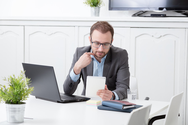 Hombre de negocios mirando el dispositivo de tableta digital en el escritorio de la oficina
 - Foto, imagen