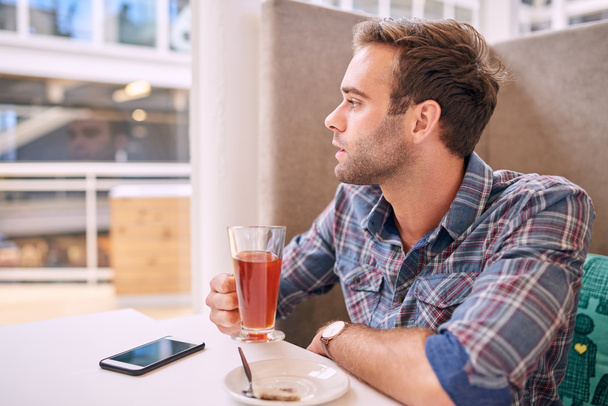 Красивий чоловік дивиться вбік, тримаючи чай в кафе
 - Фото, зображення