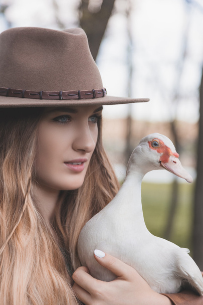 Portret dziewczynki, która trzyma biały kaczka. Ptak jest patrząc bezpośrednio na aparat. - Zdjęcie, obraz