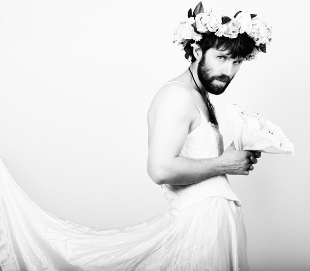 bearded man in a womans wedding dress on her naked body, holding a flower. on his head a wreath of flowers. funny bearded bride, black and white - 写真・画像