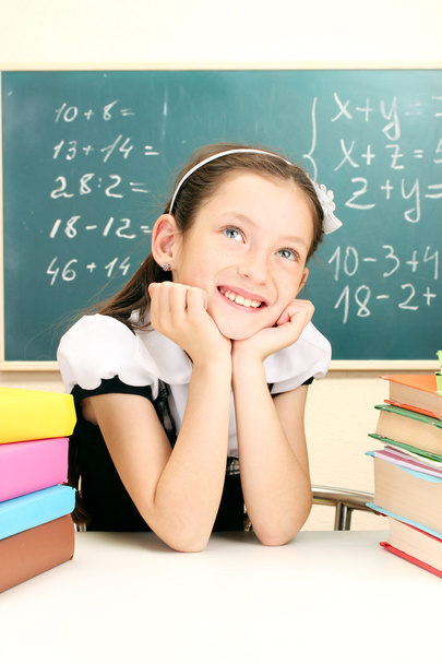 Little schoolgirl and books in classroom near blackboard - Zdjęcie, obraz