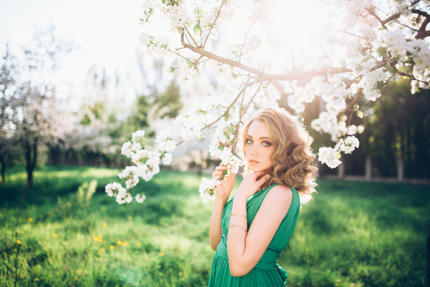beautiful young blond woman standing beside a blossoming Apple tree - Фото, изображение