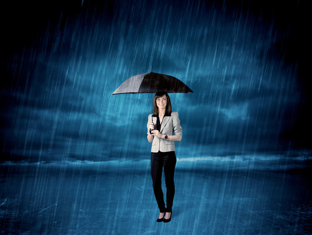 Business woman standing in rain with an umbrella - Фото, изображение