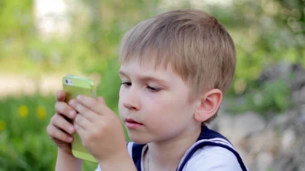 Young little boy plays games on smartphone. Spring park - Footage, Video