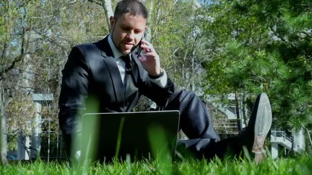 Επιχειρηματίας λειτουργεί με φορητό υπολογιστή και κινητό τηλέφωνο στο πάρκο της πόλης - Πλάνα, βίντεο