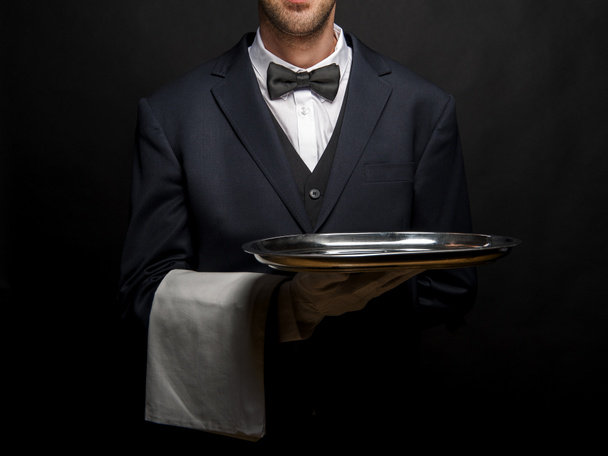 Číšník v černém obleku drží podnos na černém pozadí. - Fotografie, Obrázek