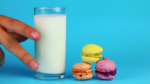 Sklenici mléka a zákusek makarónek na modrém pozadí - Záběry, video