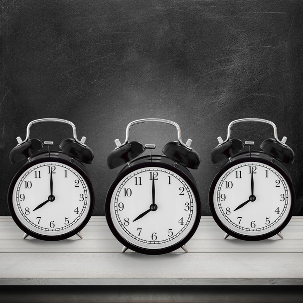 Tres de los relojes de alarma antiguos en el escritorio de la mesa de madera sobre fondo de tablero de tikboard (reloj de alarma mostrar 8 de la tarde. ) - Foto, imagen