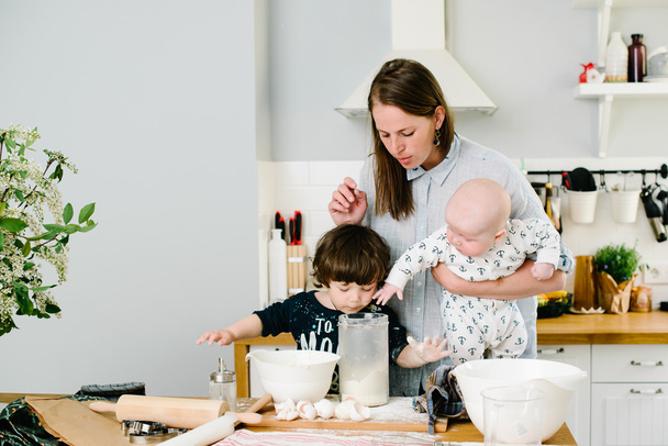 Young and happy mom with her children in the kitchen cook cookie - 写真・画像