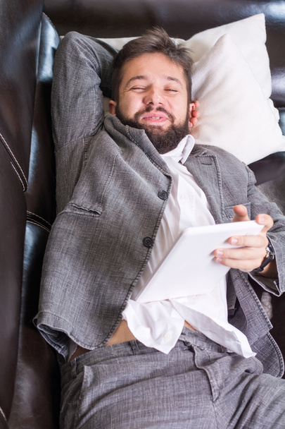 Sleepy zakenman met een tablet-apparaat - Foto, afbeelding