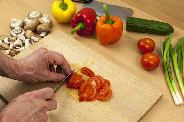 Close up van een chef-koks handen snijden een salade tomaat - Foto, afbeelding