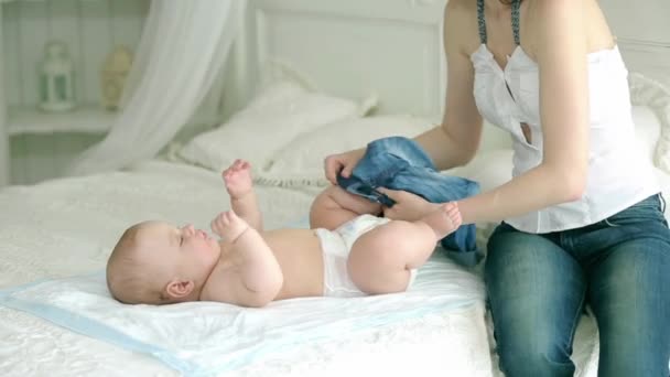 Matka se obléká dítě. Mladá matka a dítě šest měsíců. Máma nosí plenky, džíny a košili, ponožky. - Záběry, video