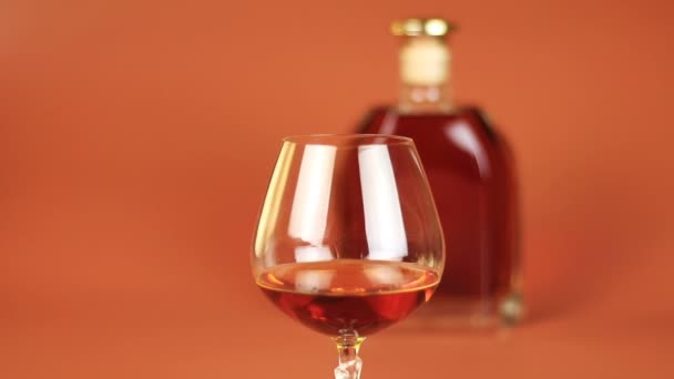 Butelkę i kieliszek brandy na brązowym tle - Materiał filmowy, wideo