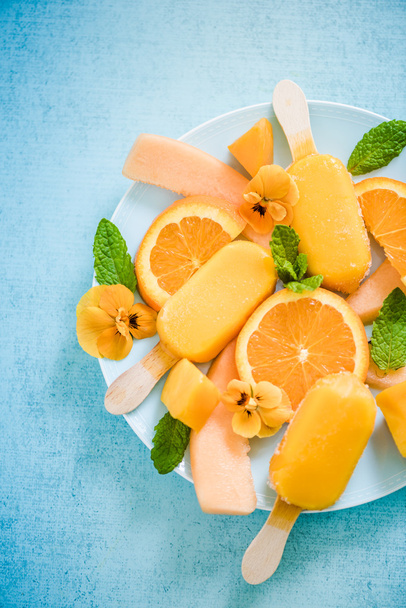 Homemade summer treat orange popsicles with fresh fruits and edible flowers - Photo, Image