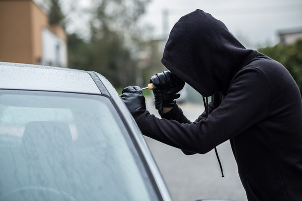 Car thief trying to break into a car with a screwdriver. - Foto, Imagem
