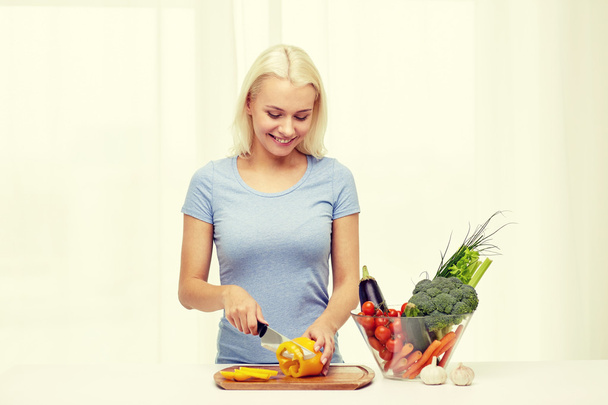 smiling young woman chopping vegetables at home - Fotografie, Obrázek