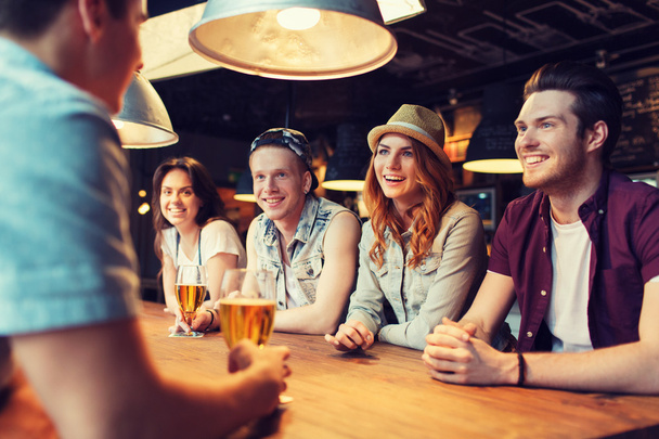 happy friends drinking beer and talking at bar - Фото, зображення