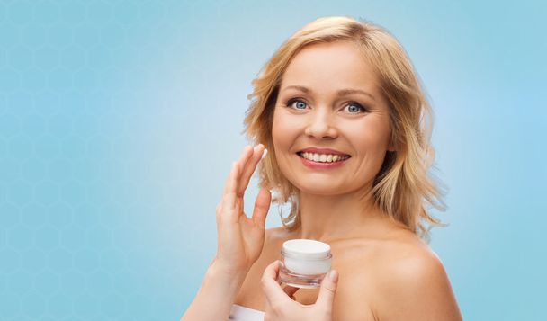 happy woman applying cream to her face - Zdjęcie, obraz