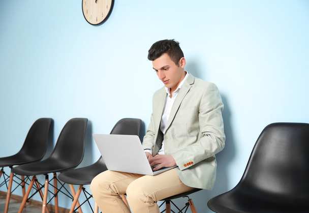 Νεαρός άνδρας στο κοστούμι κάθεται σε καρέκλα και να περιμένουν για συνέντευξη για δουλειά - Φωτογραφία, εικόνα