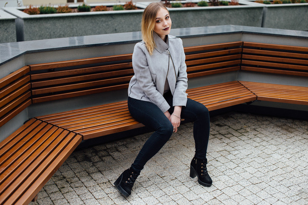 Young woman sitting on the bench in front of buindings - Fotografie, Obrázek