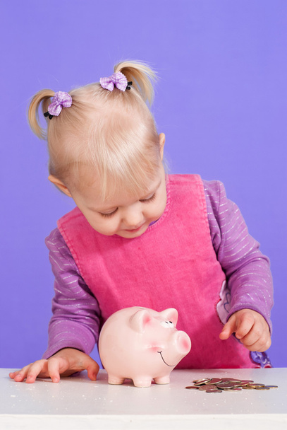 Una pequeña chica caucásica encantadora juega con moneybox
 - Foto, Imagen