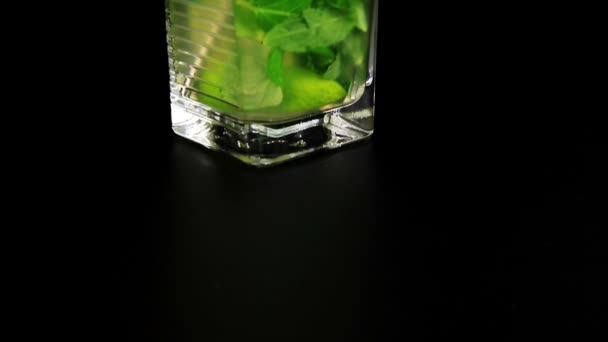 Mojito cocktail with fresh limes, mint and ice cubes on black background - Footage, Video