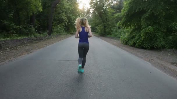 sexy athletische blonde Mädchen läuft auf der Straße im Wald. Schuss mit Schwebestativ - Filmmaterial, Video