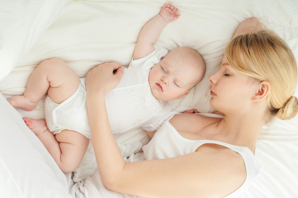 若い母親とベッドで寝ている赤ちゃん - 写真・画像