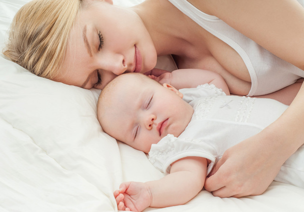 Young mother and her baby sleeping in bed - Фото, изображение