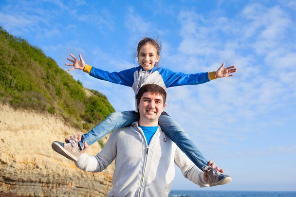 girl sitting on dad's shoulders on sea background - Foto, Imagen