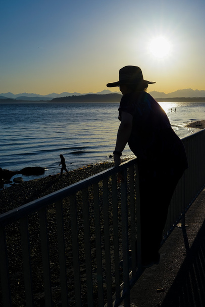 Sun tarafından korkuluk siluet duran şapkalı kadın - Fotoğraf, Görsel