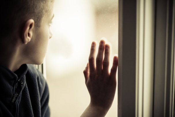 Smutny chłopiec wyglądający zewnątrz trzymając szybę - Zdjęcie, obraz
