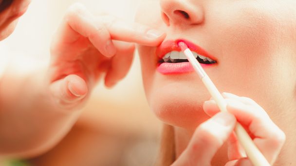 Make up artist applying lipstick with brush. - Foto, imagen