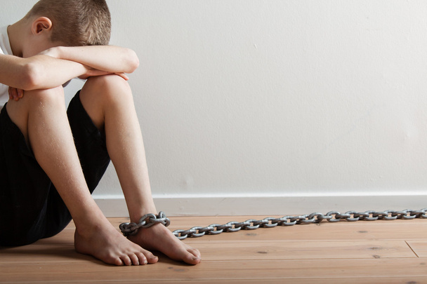 Одинокий мальчик с цепью на ноге, прячущий свою ногу
 - Фото, изображение