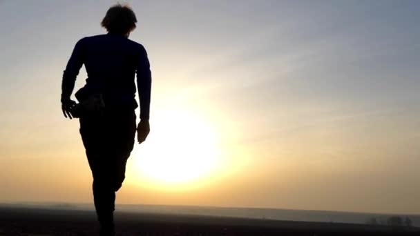Mies juoksee pellolla auringonnousun aikaan. Hidas liike
. - Materiaali, video