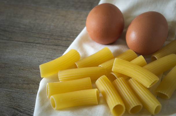 Włoskie jedzenie. Makaron (rigatoni) z jaj na drewnianym stole w słabym świetle - Zdjęcie, obraz